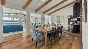 Un comedor amplio con una mesa y sillas de madera, una chimenea de ladrillo y ventanas grandes que ofrecen vistas al exterior.