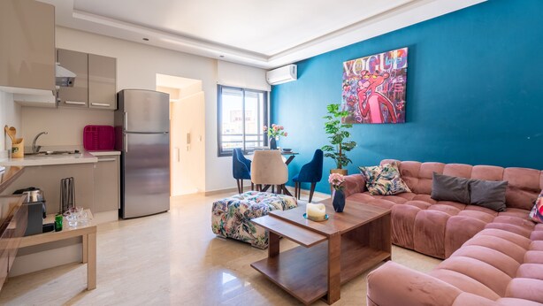 Ein modernes Wohnzimmer mit einem rosafarbenen Sofa, einem Holztisch und einer blauen Wand mit einem farbenfrohen Gemälde.
