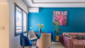 Ein modernes Wohnzimmer mit blauer Akzentwand, einem Essbereich mit rundem Tisch und Stühlen sowie einem großen Gemälde.