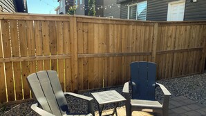 Un patio con dos sillas Adirondack y una mesa pequeña, rodeado por una cerca de madera.