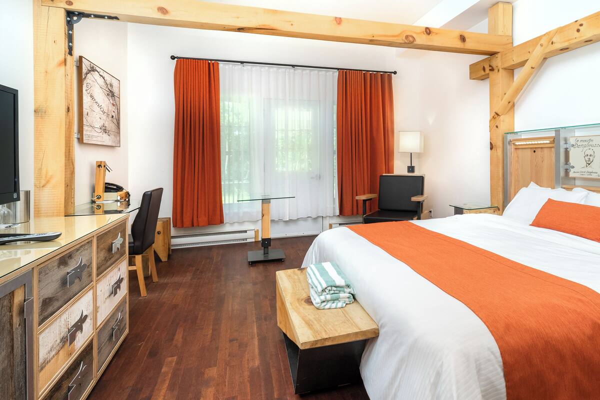 A hotel room with a bed, a desk with a chair, a TV, and a window with curtains.