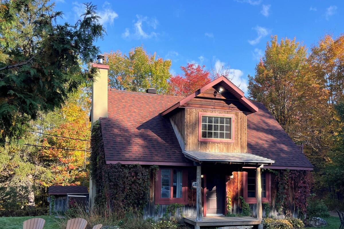 A rustic cabin with a chimney, wooden exterior, and a porch with Adirondack chairs.