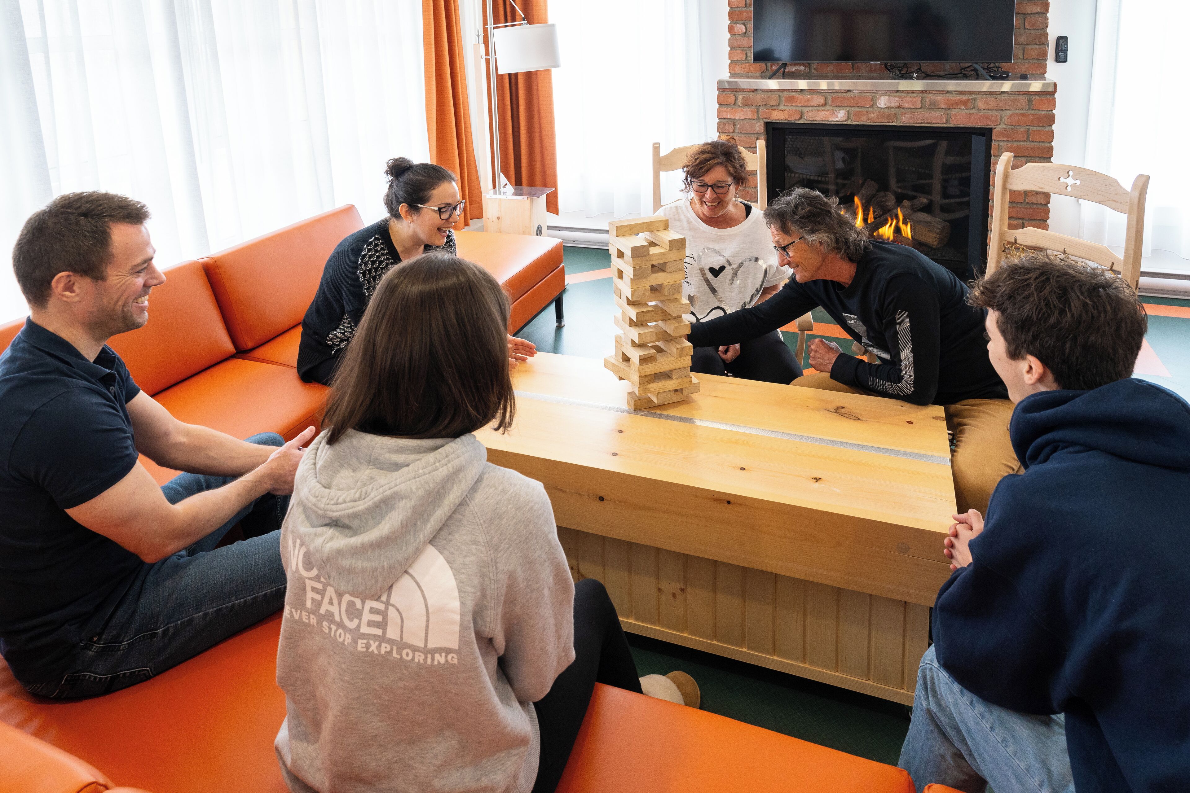 Un grupo de personas jugando un juego de mesa en una habitación acogedora con chimenea, muebles anaranjados y ambiente relajado.
