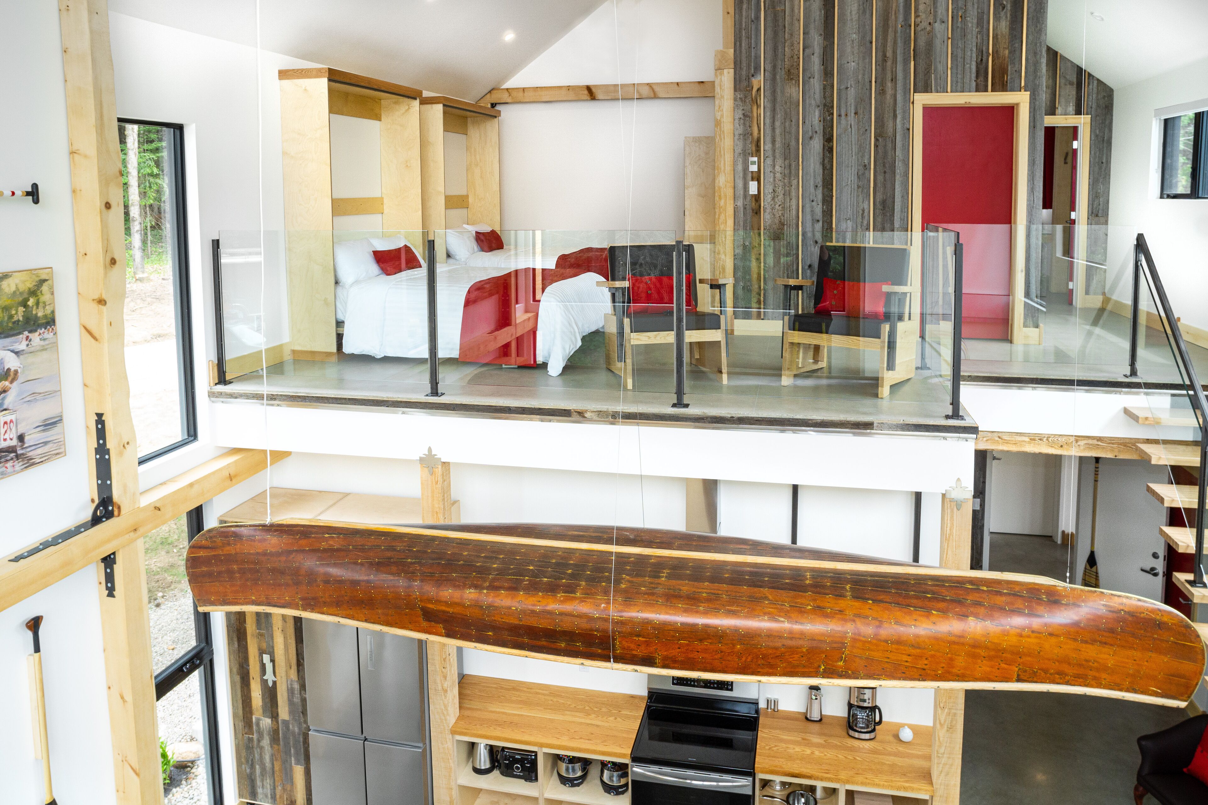 Un interior moderno con un barco de madera grande, una cama con almohadas rojas y una barandilla de vidrio que da a un nivel inferior.