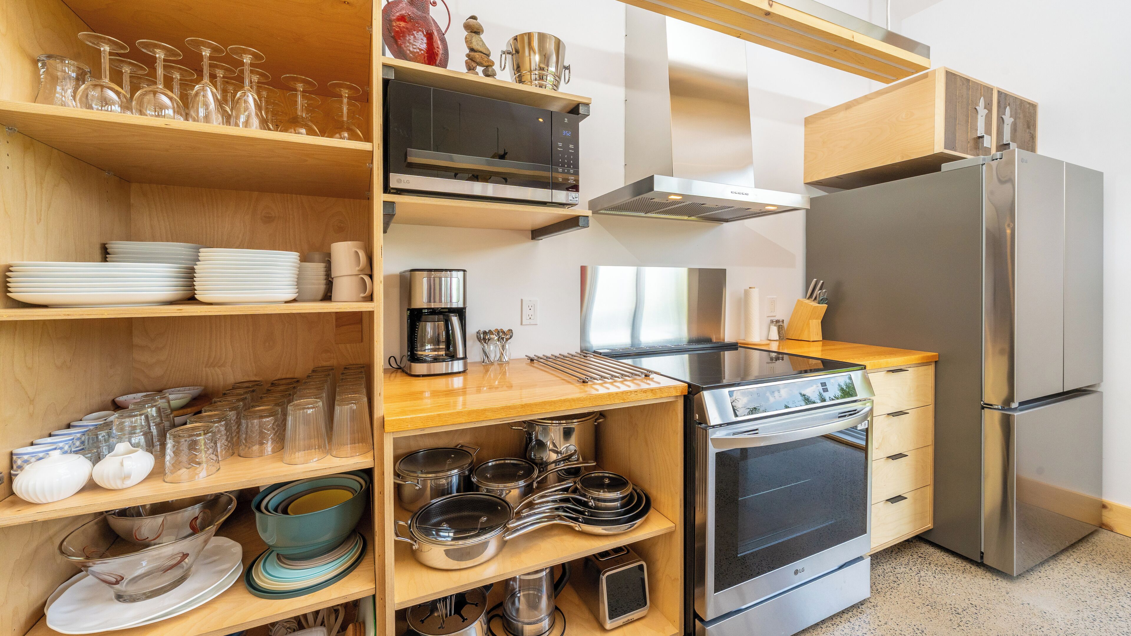 Una cocina moderna con estantes de madera, un refrigerador de acero inoxidable, un horno y diversos utensilios de cocina.