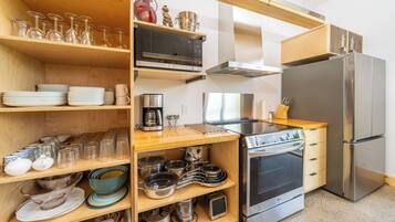 Una cocina moderna con estantes de madera, un refrigerador de acero inoxidable, un horno y diversos utensilios de cocina.