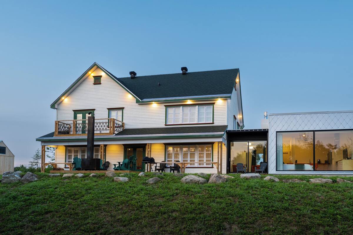 A two-story house with a balcony, a separate glass-enclosed room, and a patio area with outdoor furniture.
