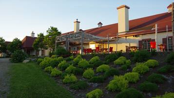A building with a covered patio area, red chairs, and a landscaped garden with neatly trimmed bushes.
