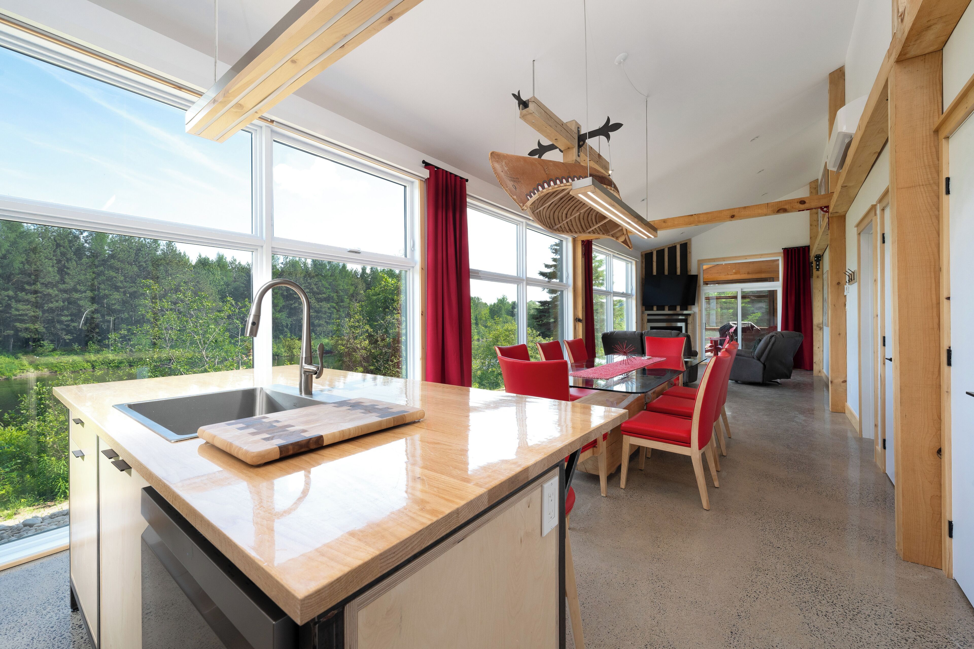 Een moderne keuken met een groot raam, een houten eiland en een eethoek met rode stoelen.