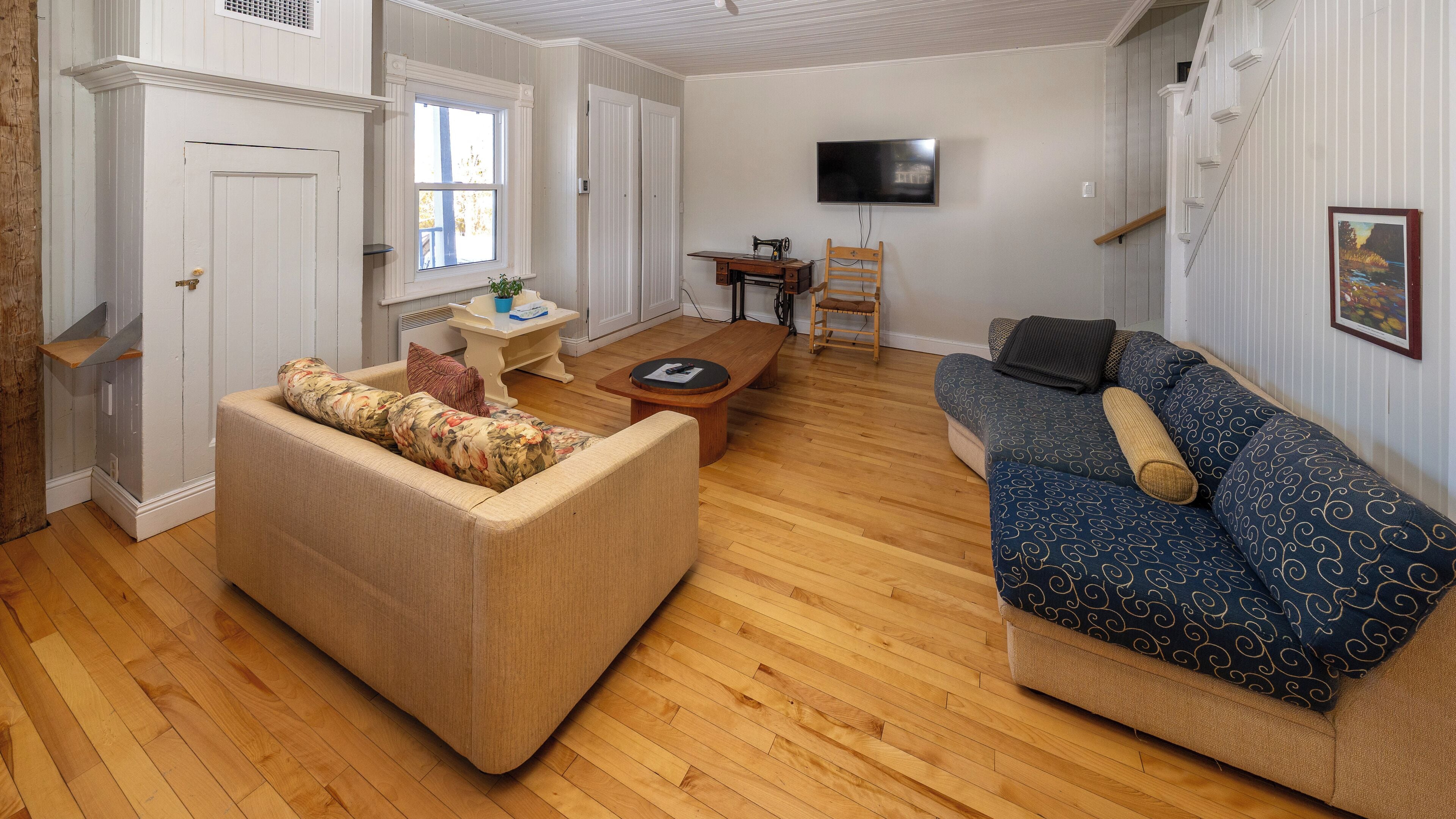 A living room with a sofa, a chair, a table, and a television mounted on the wall.