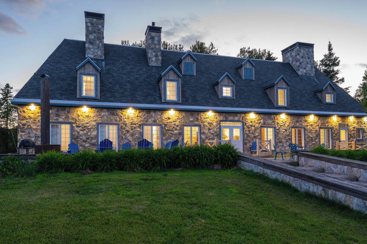 A stone house with multiple chimneys, a stone exterior, and a well-lit front porch with outdoor seating.