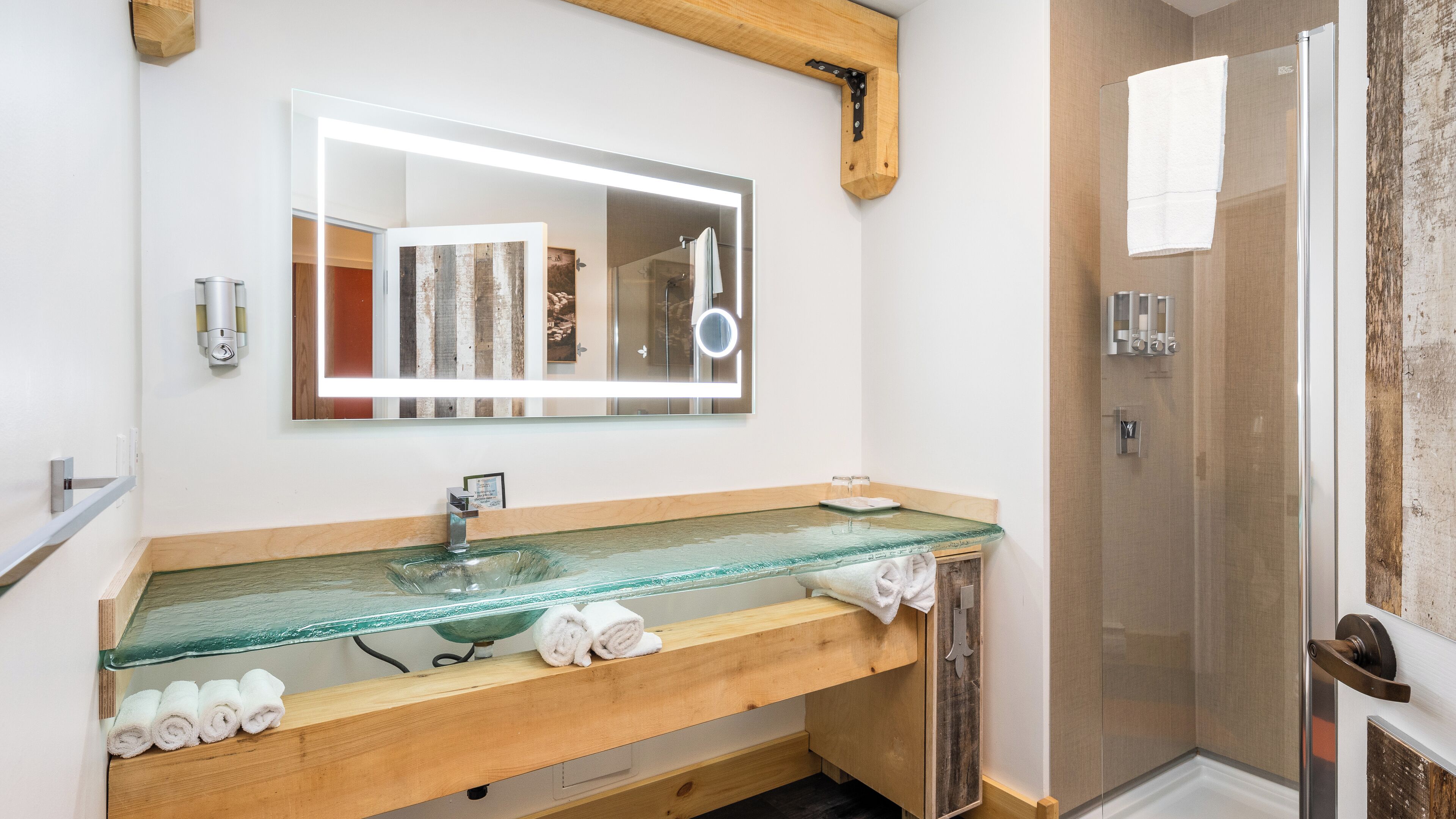 Ein Badezimmer mit einem Glaswaschbecken, einem Holzkosmetikschrank, einem großen Spiegel und einer Duschkabine aus Glas.