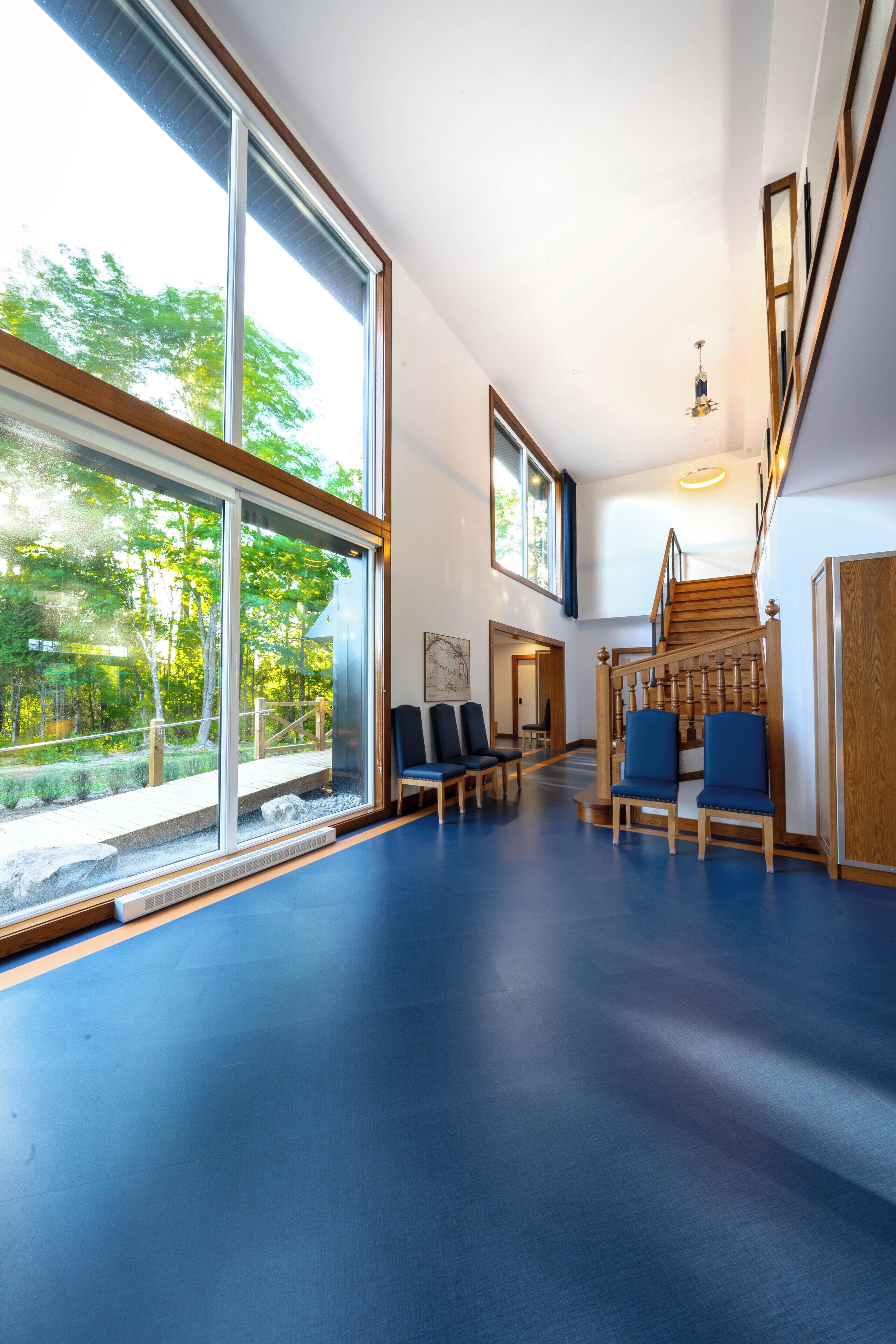 A spacious interior with large windows, a wooden staircase, and blue chairs.