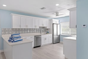 Une cuisine moderne avec des armoires blanches, un réfrigérateur en acier inoxydable et un ventilateur de plafond.