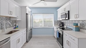 Una cocina moderna con armarios blancos, un refrigerador de acero inoxidable, un microondas y un ventilador de techo.