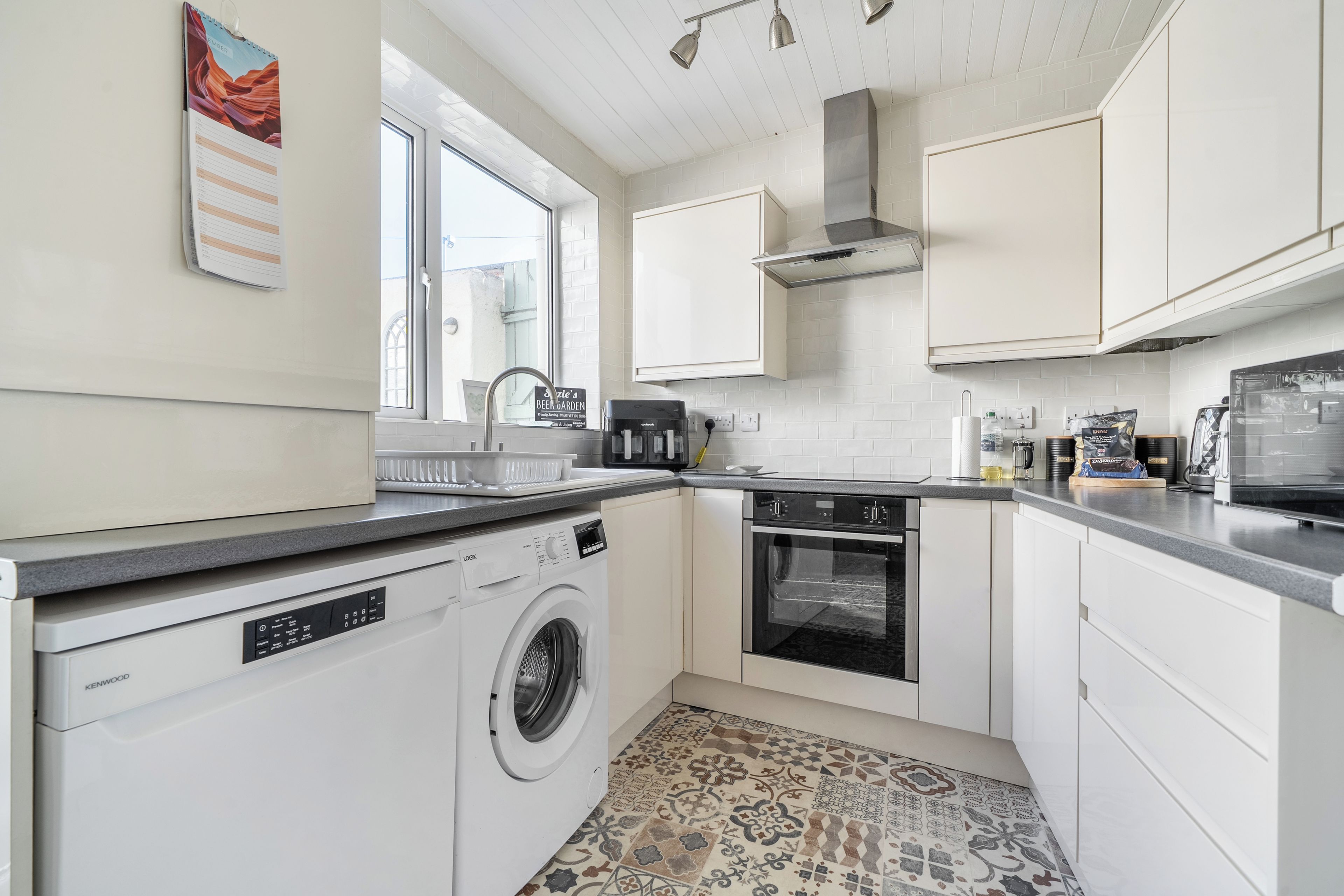 A modern kitchen with a built-in washing machine, oven, and a window providing natural light.