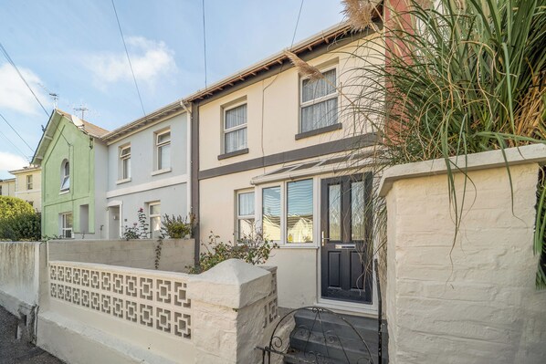 A two-story residential building with a front door, windows, and a small garden area with plants. - Torquay 3-bed House, Sleeps 6, Pets Ok & Parking (Torquay)