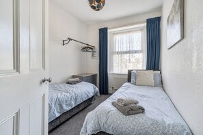 A bedroom with two beds, a wardrobe, a radiator, and a window with curtains.