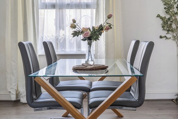 A modern dining table with a glass top and wooden legs, surrounded by four grey upholstered chairs.