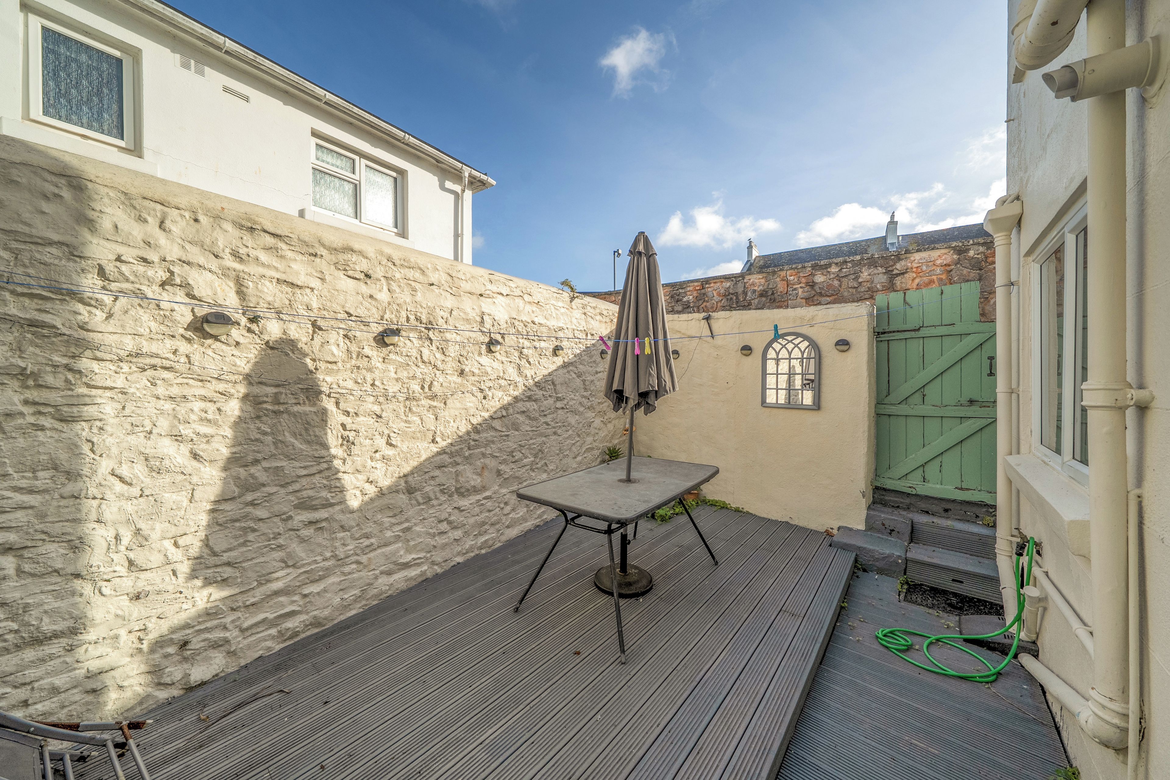 A courtyard with a metal table and chairs, a green gate, and a stone wall.