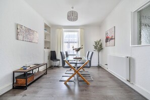 A modern dining area with a glass table, black and gray chairs, a wooden bench, and a radiator. - Torquay 3-bed House, Sleeps 6, Pets Ok & Parking (Torquay)