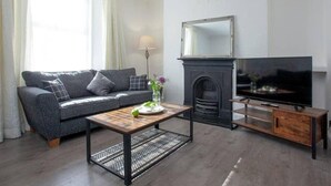 A modern living room with a grey sofa, a wooden coffee table, a fireplace, and a TV.