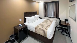 Habitación de hotel con una cama grande, un escritorio, una silla, un televisor y un ventanal con cortinas.