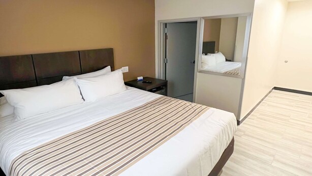 Habitación de hotel con una cama grande, una mesita de noche, un espejo y una puerta que da a un armario.