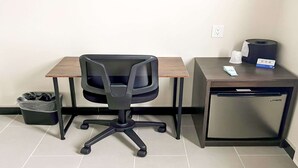 Un petit bureau comprenant un bureau, une chaise, une poubelle et un petit réfrigérateur.