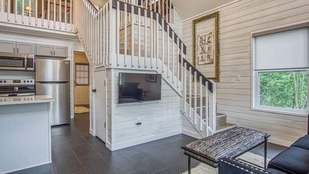 A spacious living area with a modern kitchen, a staircase leading to an upper level, and a large window offering a view of the outdoors.