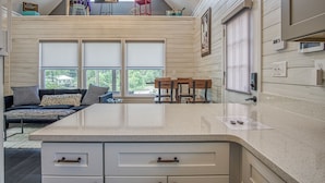 A modern kitchen with a large island, a dining area with a sofa and chairs, and a view of the outdoors through large windows.