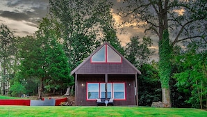 A house with a triangular roof, a stone wall in front, and a grassy lawn.