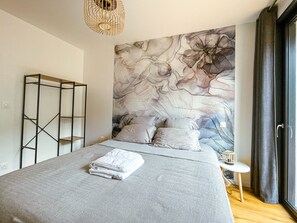 A bedroom with a large bed, a wall-mounted shelf, and a window with curtains.