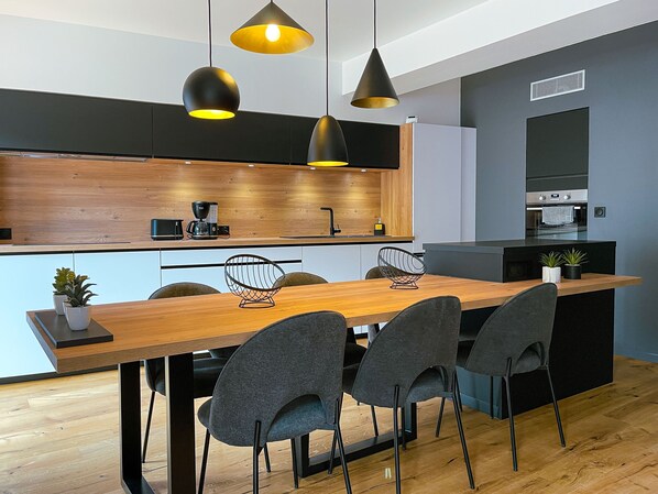 A modern kitchen with a wooden island, black pendant lights, and a built-in oven.