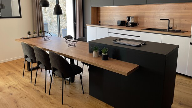 A modern kitchen with a wooden island, black cabinets, and pendant lighting.