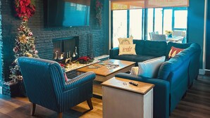 Een gezellige woonkamer met een open haard, een blauwe bank, een gestreepte fauteuil en een kerstboom.