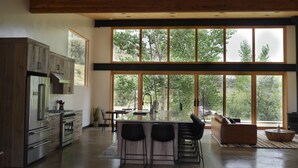 A modern kitchen with a large island, bar stools, and a dining area with a view of trees.