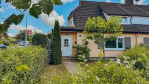 Une maison à deux étages, avec un toit recouvert de tuiles, une porte blanche et une petite fenêtre.