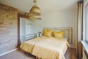 A bedroom with a brick wall, a bed with yellow bedding, a wicker pendant light, and a white wardrobe.