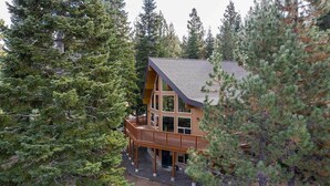 A wooden cabin with a balcony, surrounded by dense evergreen trees.