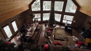 A spacious room with a high ceiling, large windows, a dining area, a fireplace, and a Christmas tree.