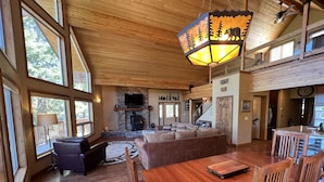 A spacious living room with a fireplace, wooden furniture, and large windows.