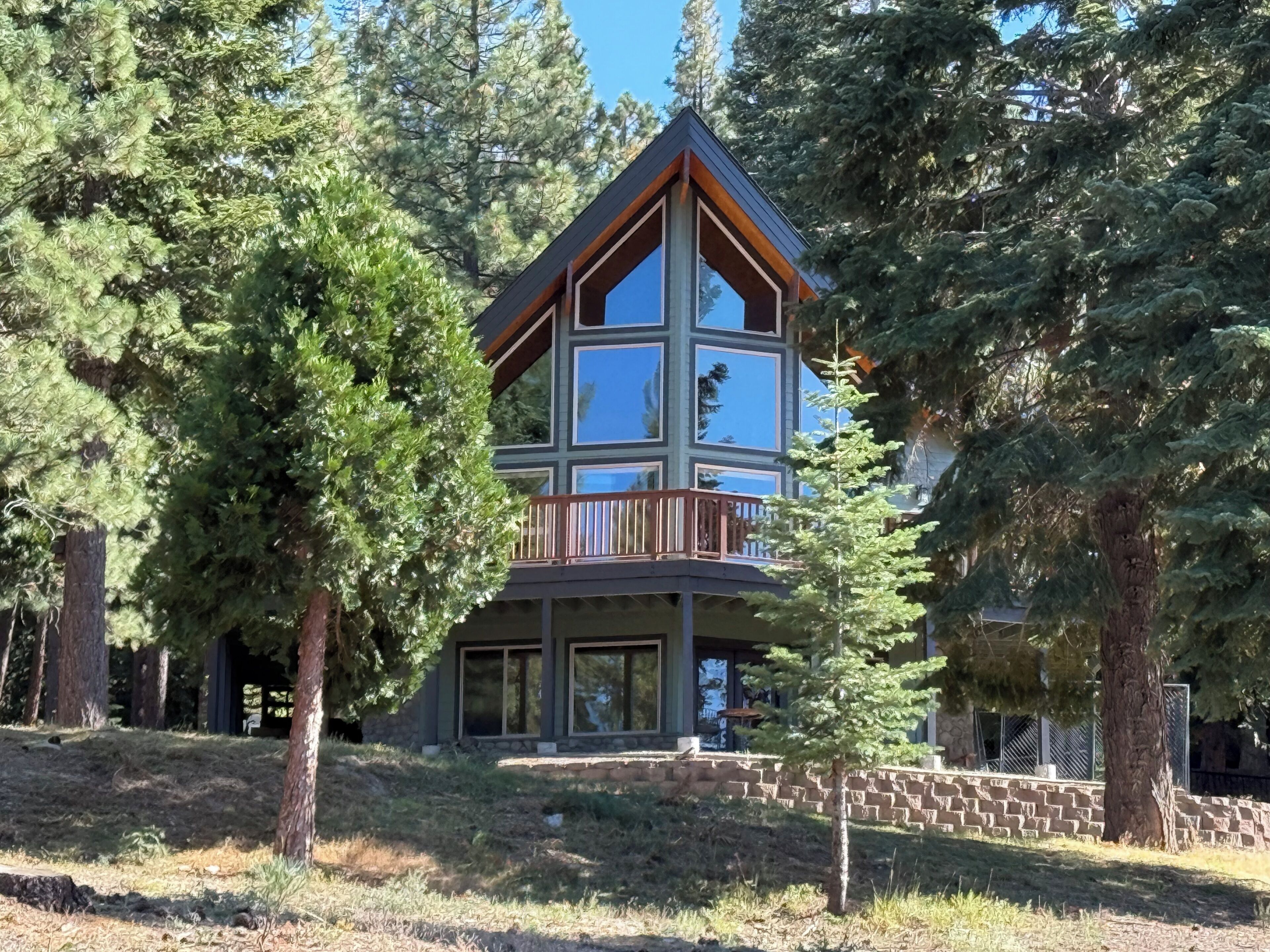 A multi-story cabin with a balcony, surrounded by trees.