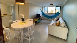 Uma sala de estar moderna com um sofá branco, uma mesa de jantar com cadeiras, uma TV e uma rede.