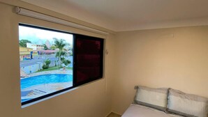 Quarto com uma grande janela com vista para uma piscina e para a paisagem urbana.