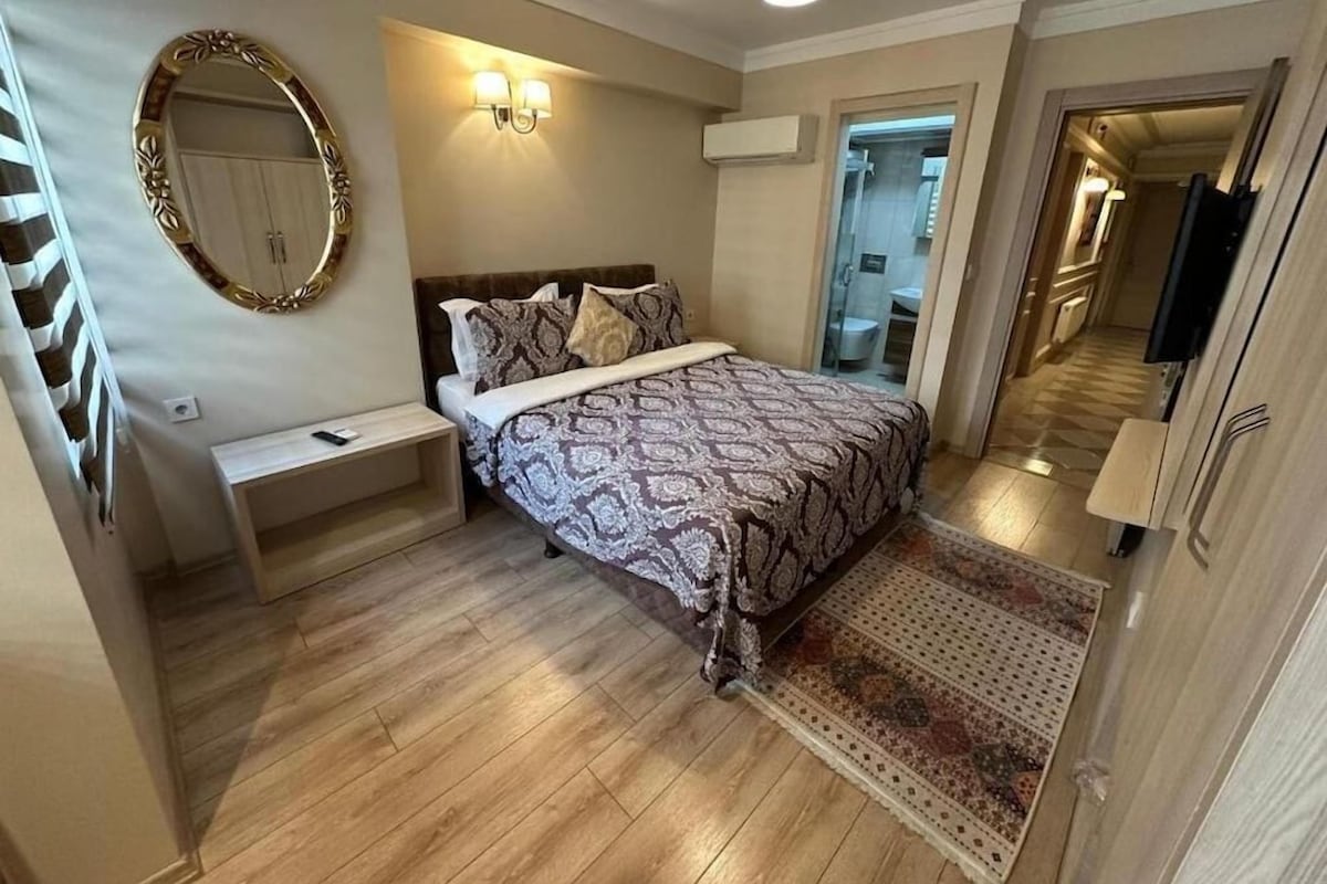 A bedroom with a bed, bedside table, wall-mounted mirror, and a light fixture.