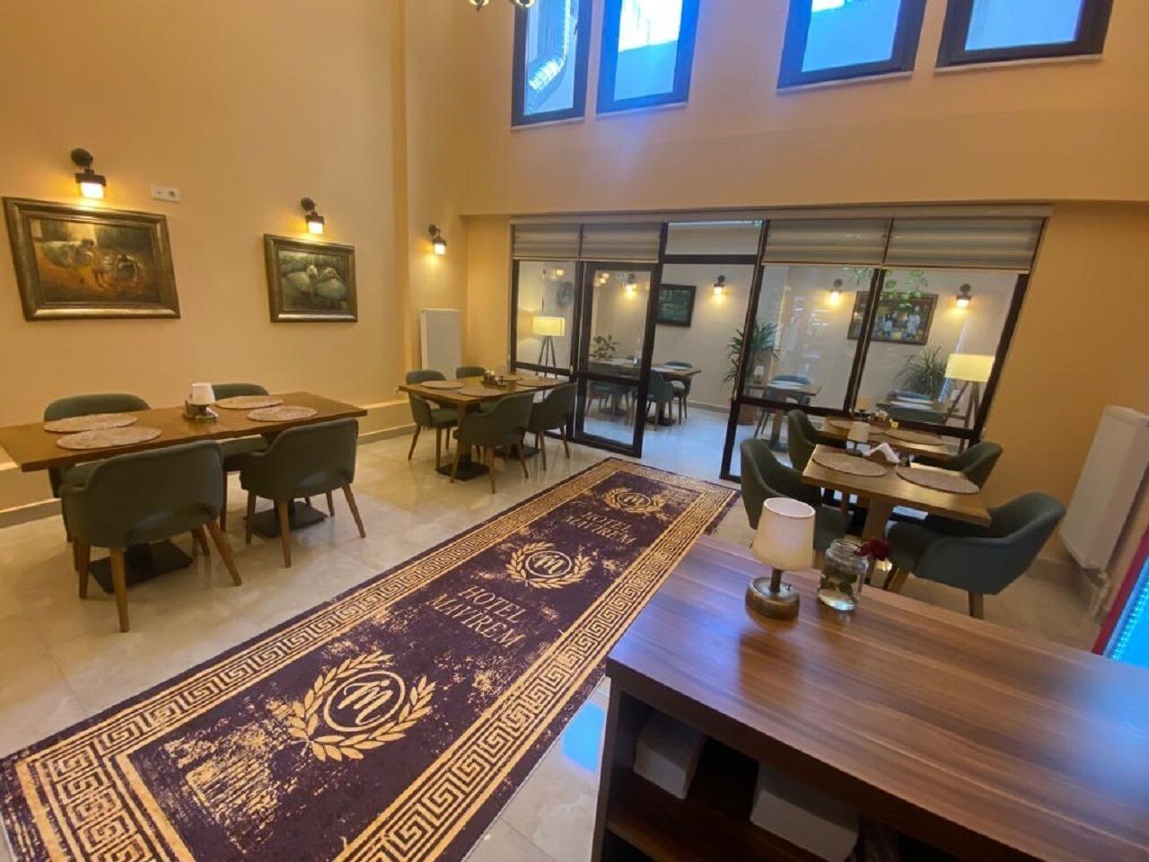 Un comedor de hotel con varias mesas y sillas, una alfombra decorativa y obras de arte en las paredes.