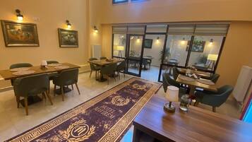 Un comedor de hotel con varias mesas y sillas, una alfombra decorativa y obras de arte en las paredes.