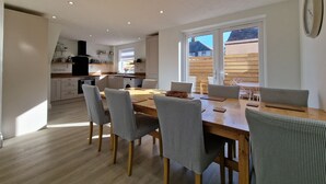A modern kitchen with white cabinets, a wooden countertop, and a built-in oven. There is a dining area with a wooden table and striped chairs.
