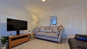 A living room with a flat-screen TV, a sofa, a wooden entertainment unit, and a door.